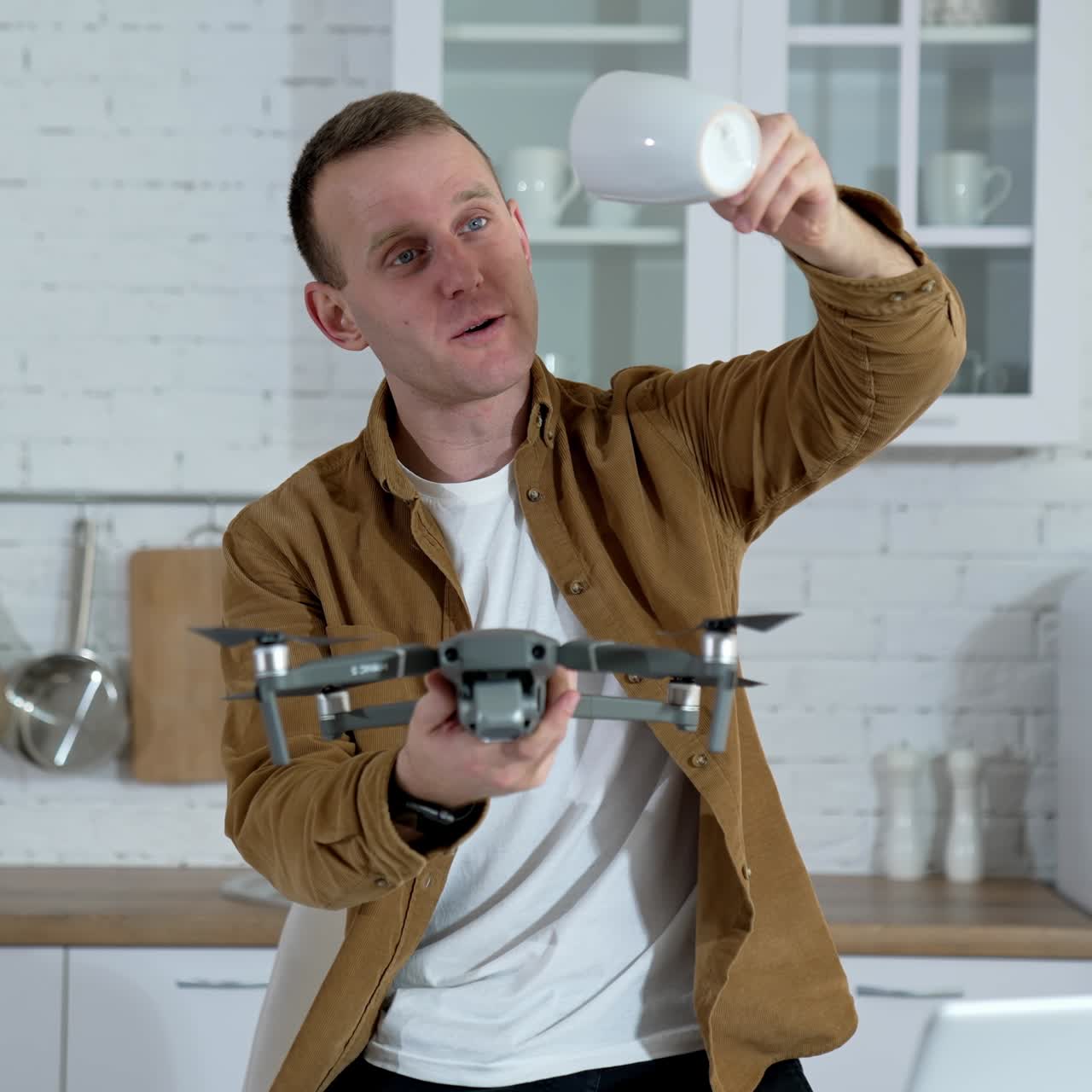Smiling man with a drone in flat. Young man holding a drone and a cup in the kitchen. Funny man with a drone indoors