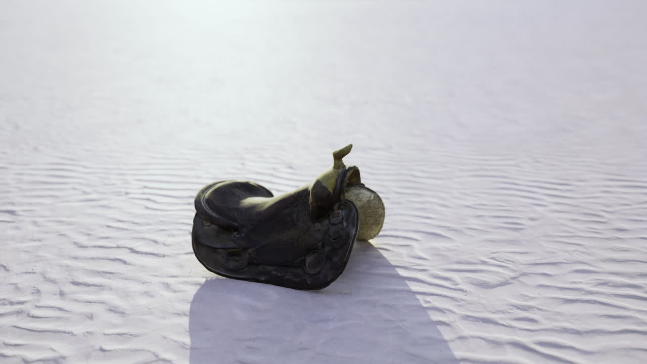Old cowboy saddle rests on sunlit desert sand under wide blue skies