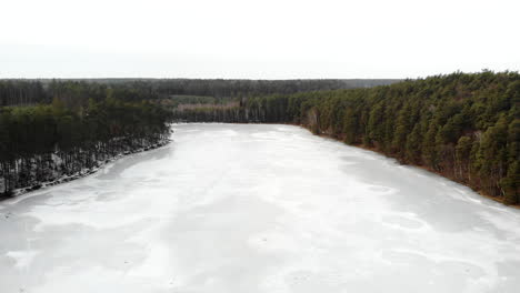 Aerial-view-on-icy-lake-in-the-middle-of-forest