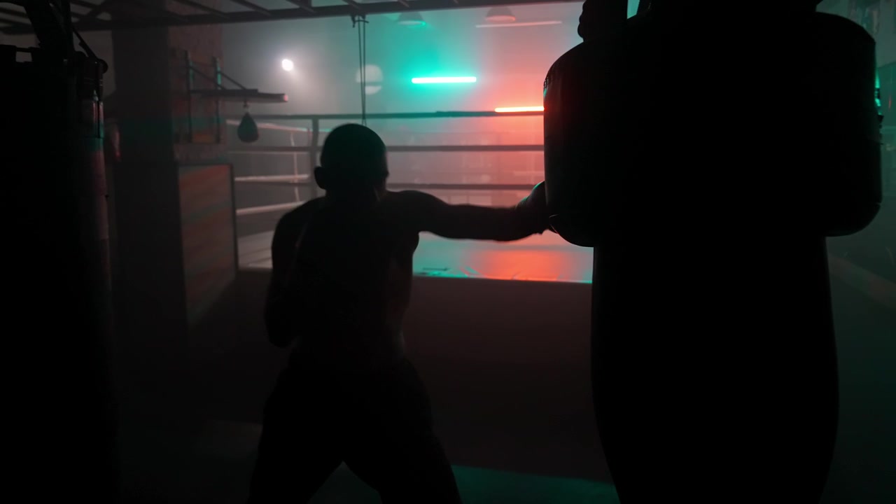 Silhouette eines Boxers beim Training am Boxsack in dunklem Fitnessstudio