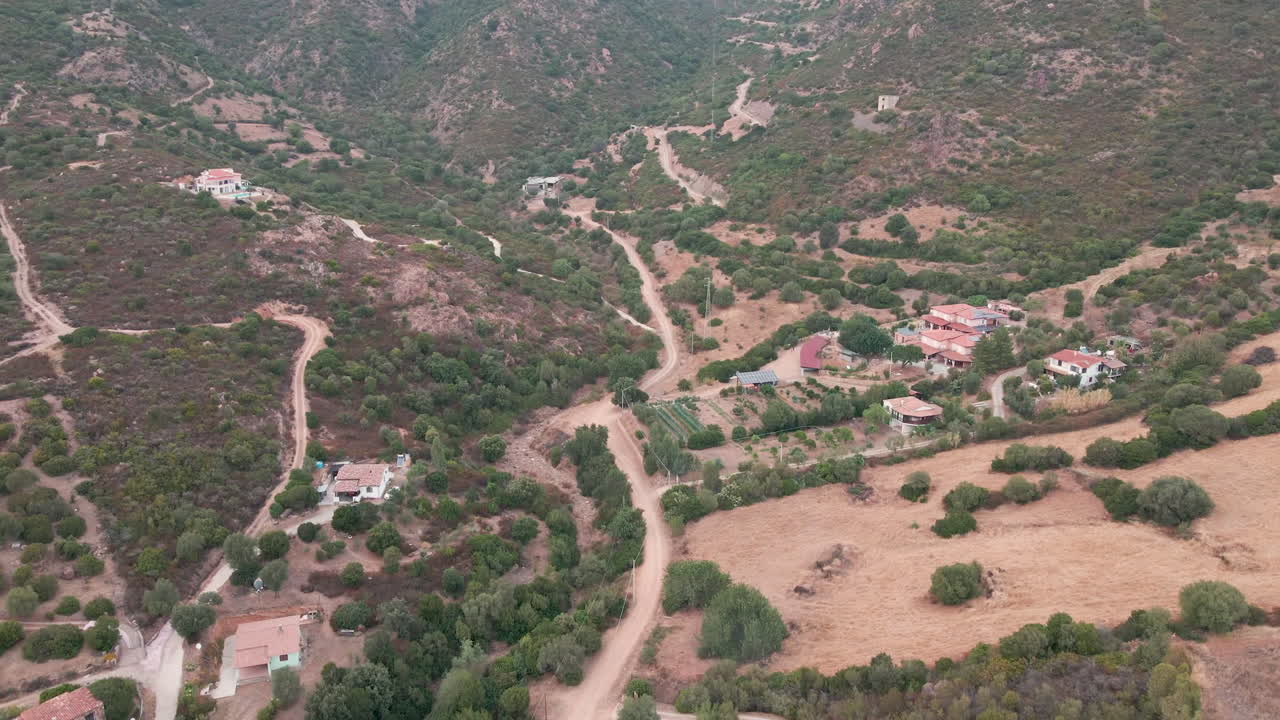 Panoramic Flight With Top View Of A Group Of Holiday Homes In The Valley Between Mountains With Mediterranean Vegetation At Sunset In Sardinia, Italy - Aerial Drone Shot
