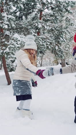 children are holding each other's hands in the yard and running up in a snowy hill together on the background of trees in the winter. slow motion vertical video