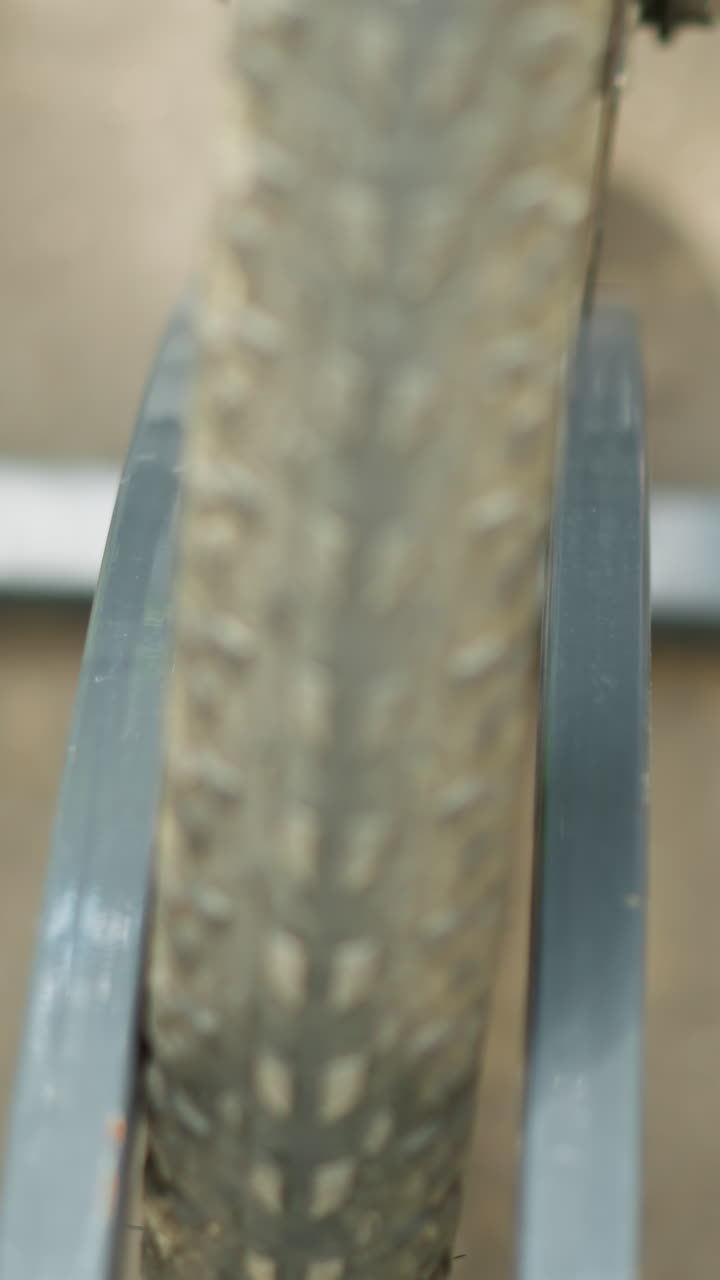 primer plano de un neumático de bicicleta trasladado a un soporte de bicicleta de metal, enfatizando la rueda, el marco y los rayos con una vista detallada contra el pavimento de alquitrán de carbón y las sombras suaves en el hormigón