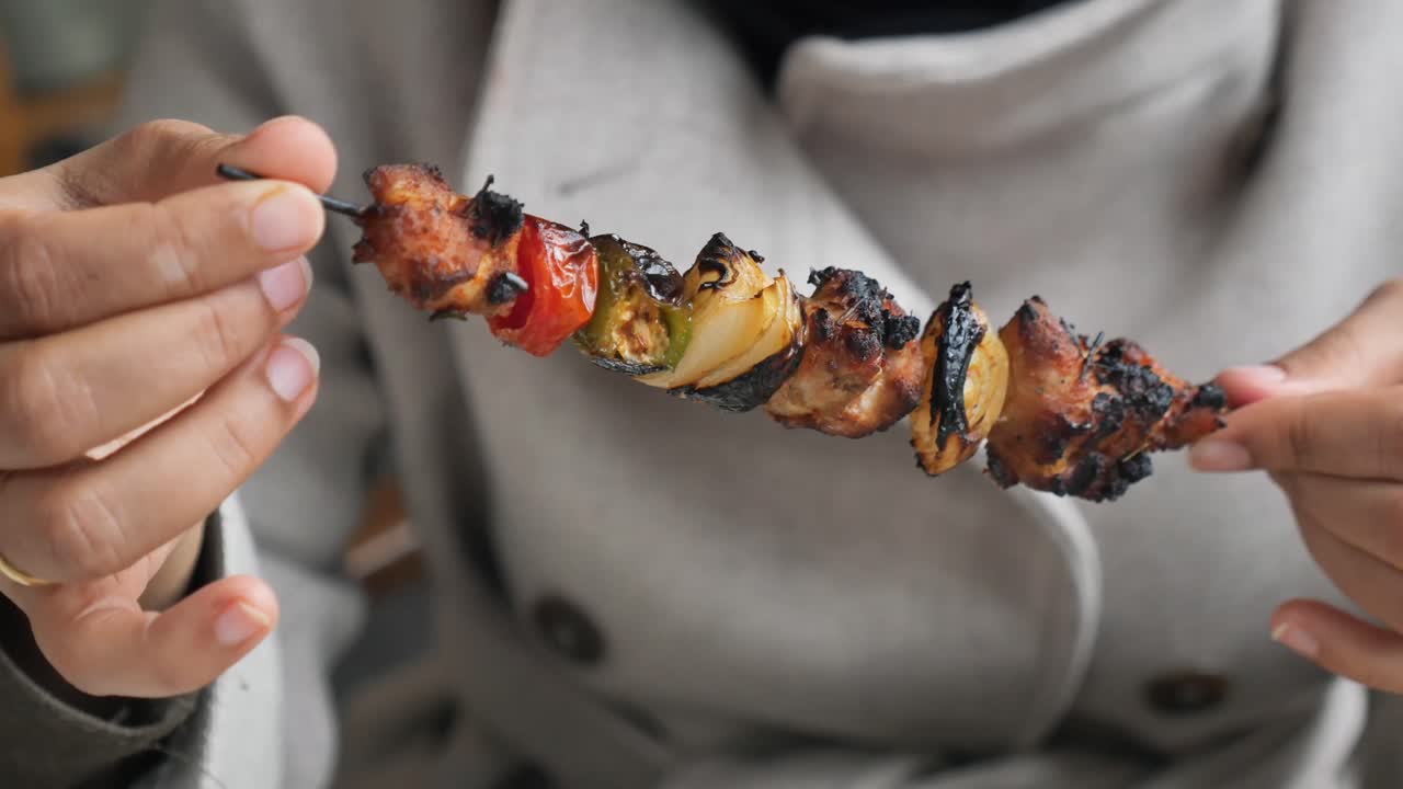 Primo piano di mani che tengono un delizioso spiedino di pollo e verdure grigliati.