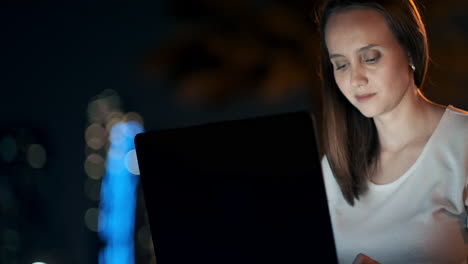 young beautiful girl designer working remotely on a laptop on the street in the summer under palm trees at night in the city park. united arab emirates european woman at night in dubai