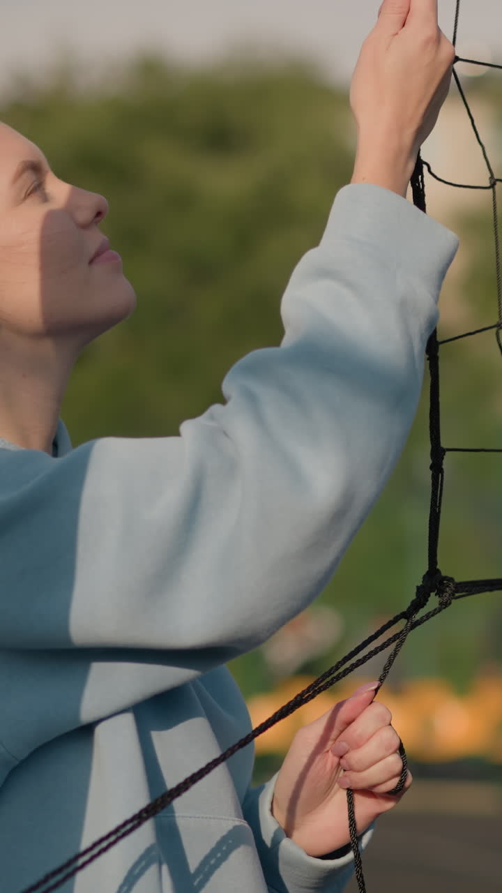 dama sosteniendo una red de voleibol con dos mujeres jugando voleibol en el fondo, otras personas en el fondo borroso distante en el campo deportivo al aire libre soleado