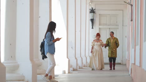adult couple in medieval costumes walks talking by the castle corridor. brunette girl in contemporary outfit appears and takes selfie. modern meets past.