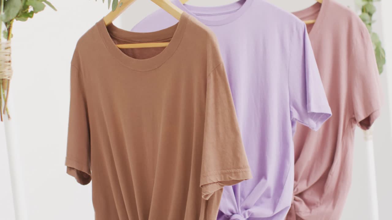 video de primer plano de camisetas blancas, beige y púrpuras colgando sobre un fondo blanco