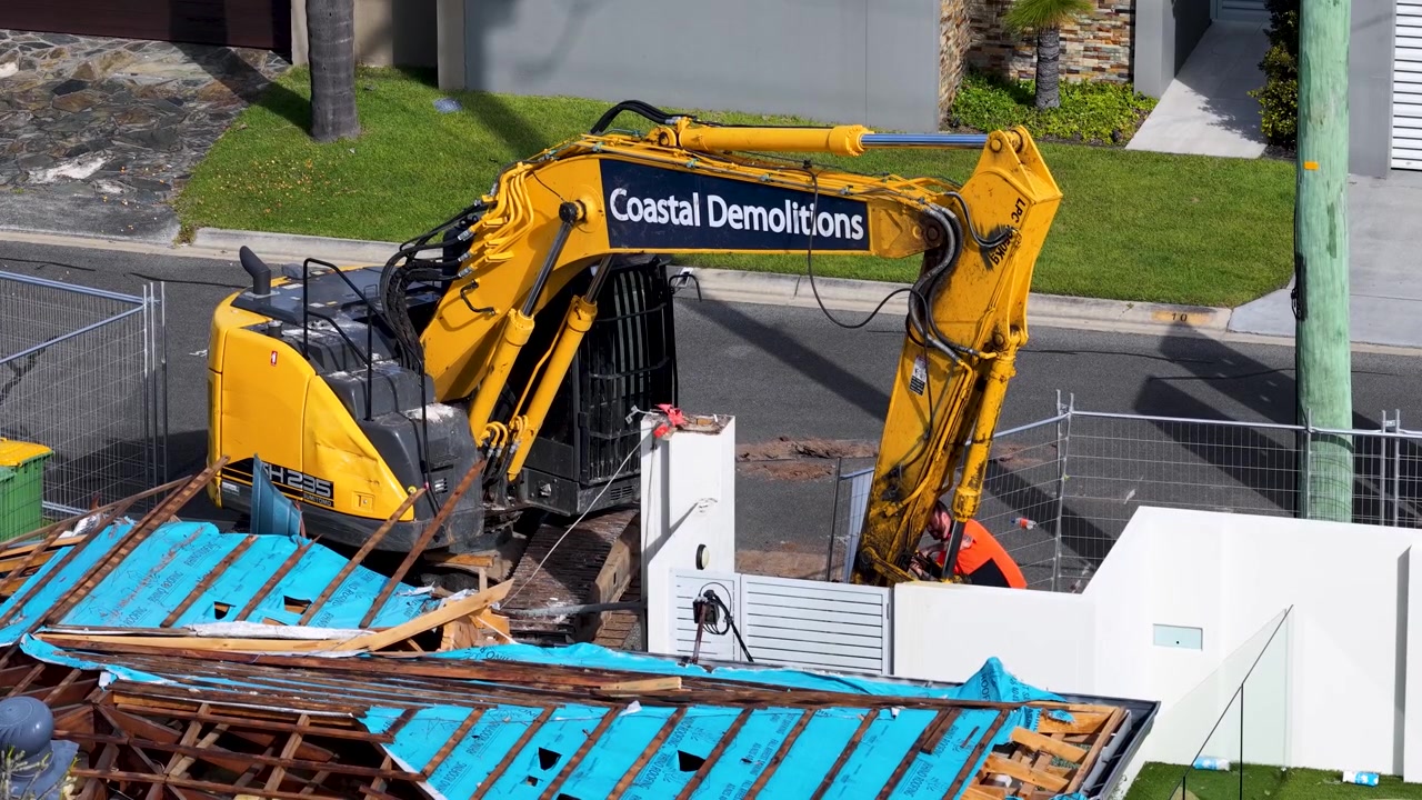 Escavadeira amarela demolindo estrutura de casa residencial