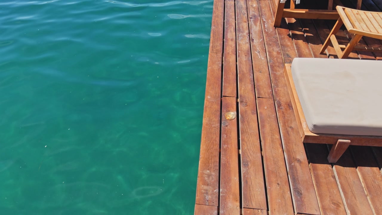 Top-down overhead shot of wooden pier edge over crystal clear Aegean water, seagrass visible on seabed below, beach club pier detail, Turkey