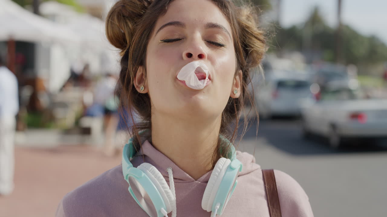 portrait of beautiful young hispanic woman blowing bubblegum bubble laughing happy enjoying relaxed summer vacation on sunny urban beachfront