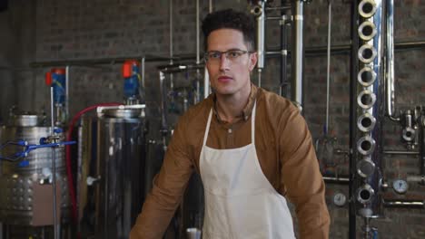 portrait of serious caucasian man working at gin distillery, using equipment and looking to camera