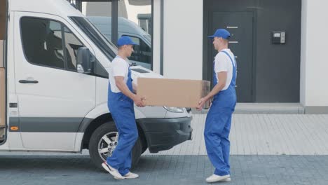 two young workers of removal company unload boxes from minibus into customer's home