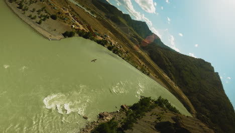 bird flies over mountain river in valley fpv. majestic eagle flight above water flow running between sloppy hills on sunny day. magnificent virgin nature