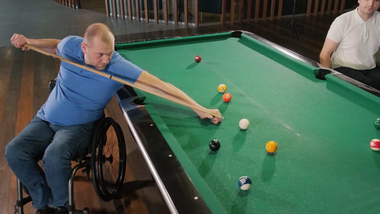 Adult men with disabilities in a wheelchair play billiards in the club