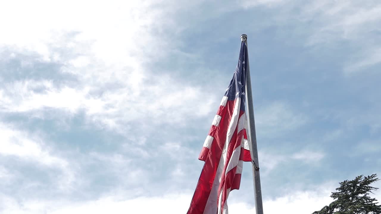 Slow motion video showing an American flag blowing in the wind slowly and dramatically revealing several flags behind it, setup for Memorial Day 2019 at a regional cemetery in California