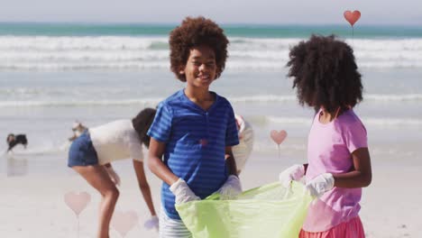 Animation-of-hearts-over-african-american-female-and-male-volunteers-picking-up-rubbish-on-beach