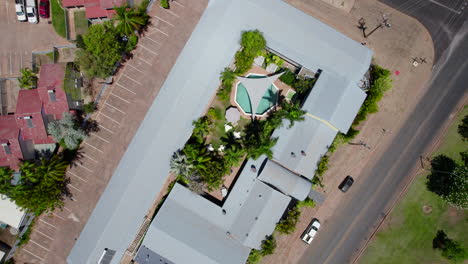 aerial drone luxurious property birds eye view of round outdoor pool tropical greenery palm trees grey shade sail, outdoor seating entertainment area, sun lounge grey roofs