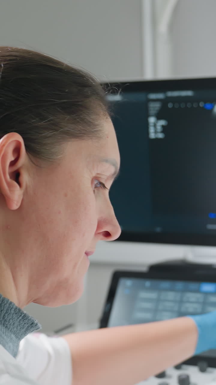 Un técnico utiliza un panel de control de ultrasonidos; perfil lateral centrado en la interfaz de la pantalla táctil y el monitor; sonda y cable apoyados en la consola; ajuste de la configuración durante la exploración en directo; entorno clínico luminoso