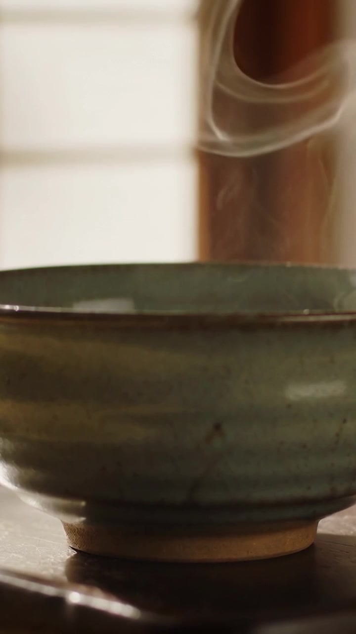 Video verticale: Vapore che si sprigiona, ciotola di ceramica verde che si raffredda su un tavolo di legno, finestra e colonna