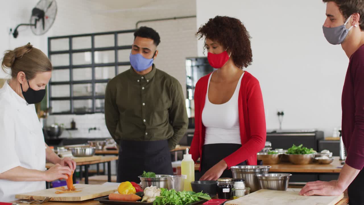 Caucasian female chef teaching diverse group wearing face masks