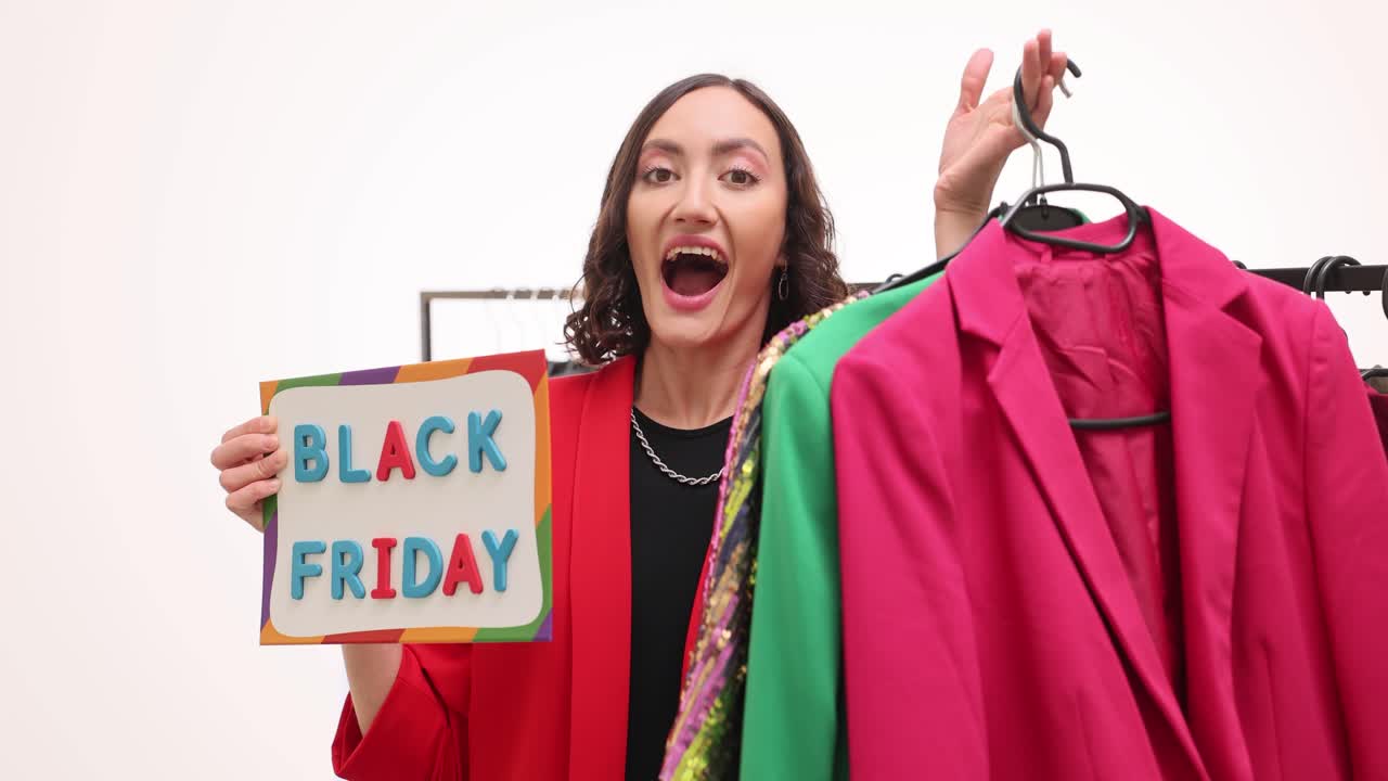 Donna entusiasta regge un cartello del Black Friday vicino a uno stender di vestiti alla moda.
