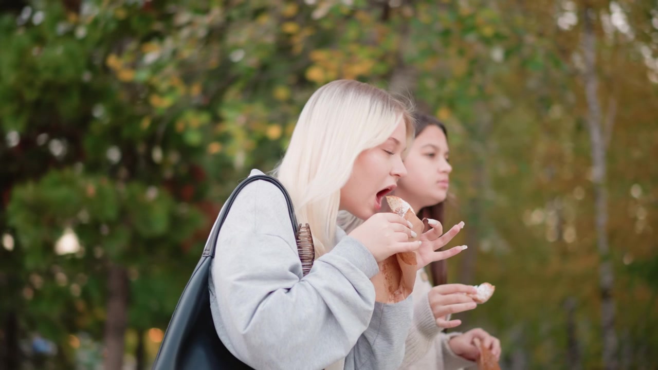 Due giovani donne che mangiano dolci all'aperto in autunno.