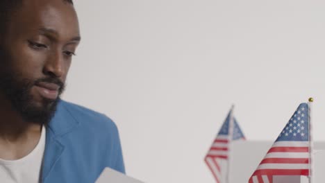 man in booth filling in ballot paper in american election casting vote into ballot box