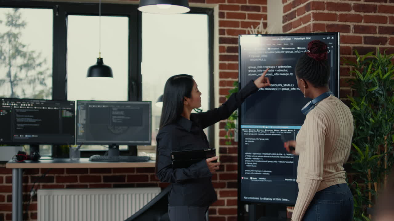 Software engineers analyzing code on wall screen tv looking for bugs and errors while colleague programer typing