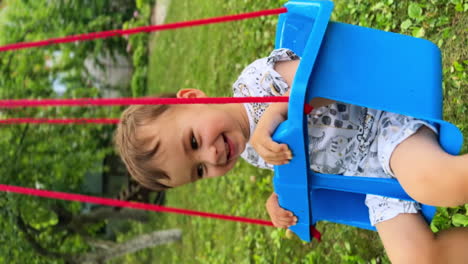 happy time spending in summer outdoors. smiling baby boy swaying on the swing. vertical screen.