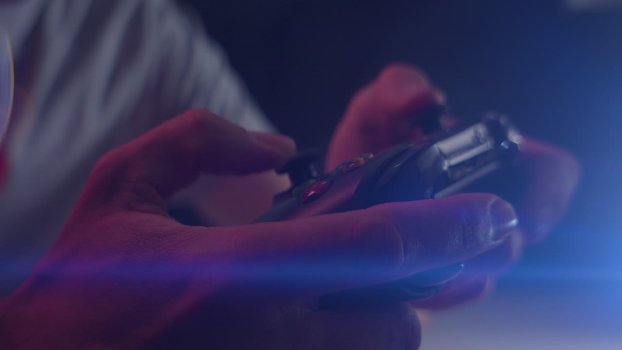 Playing video games in a darkened room with an anamorphic lens flare on a controller triggers playing quickly close up