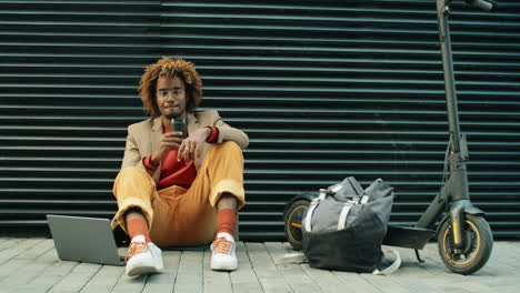 Portrait-of-African-American-Man-with-E-Scooter,-Coffee-and-Laptop-on-Street