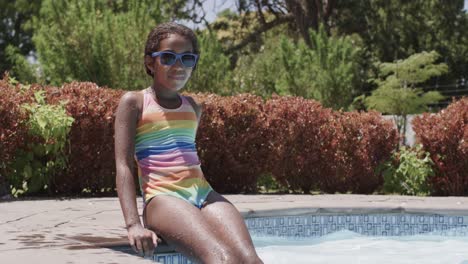 portrait of happy african american girl wearing sunglasses in swimming pool, slow motion
