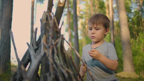 Un-Niño-De-3-A-4-Años-Ayuda-A-Poner-Palos-En-Una-Fogata-Durante-Un-Viaje-Al-Bosque-En-Familia-En-La-Naturaleza.-Vacaciones-Familiares-En-El-Bosque-Con-Tiendas-De-Campaña