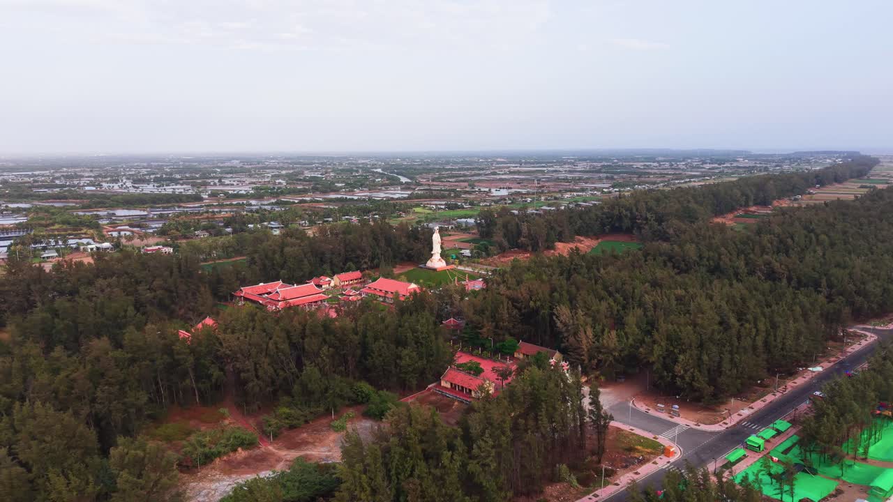 Visita a una gran estatua en Tra Vinh, Vietnam, rodeada de naturaleza y edificios a la distancia.