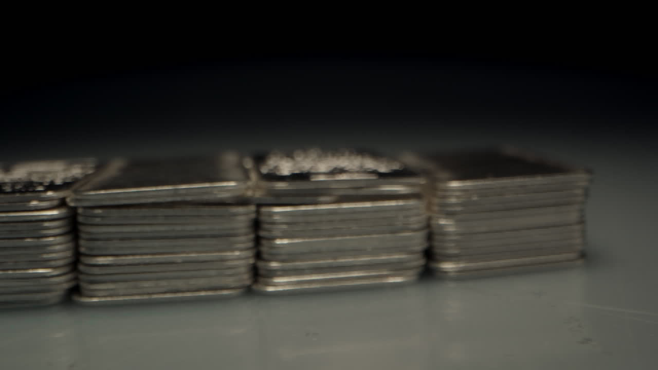 Cinematic macro dolly of many stacks of silver bars lit by a spotlight in a dark room