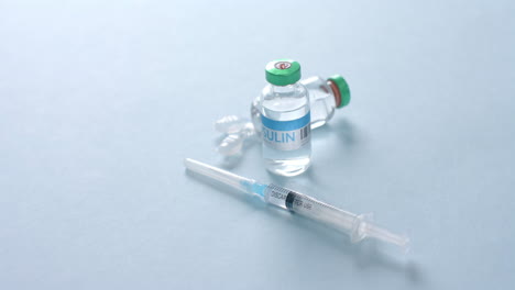close up of insulin vials and syringe on blue background with copy space, slow motion