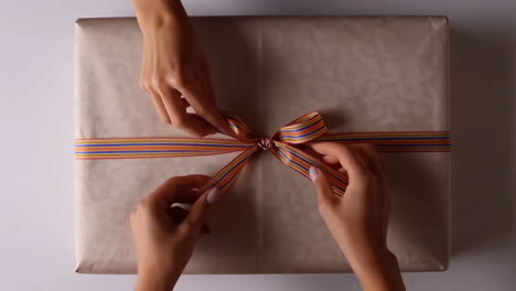 hands tying a colorful ribbon on a gift box