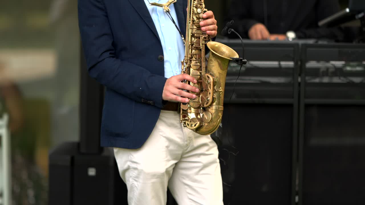 saxophonist dressed in a navy blazer and beige trousers playing an alto saxophone at an outdoor event