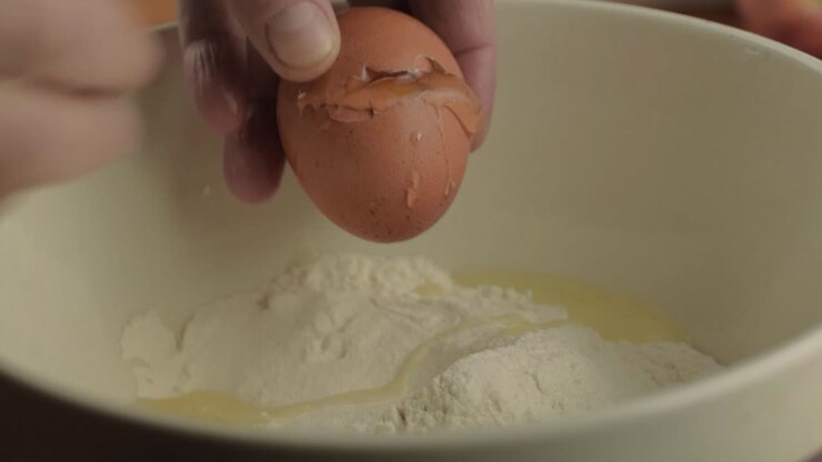 Hand cracking egg into a bowl of flour close up shot