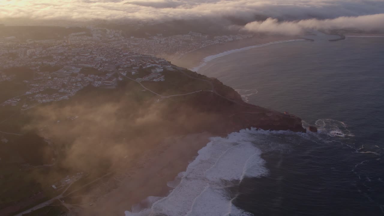 Wide shot of Nazar&eacute; town Portugal during sunrise with low clouds, aerial