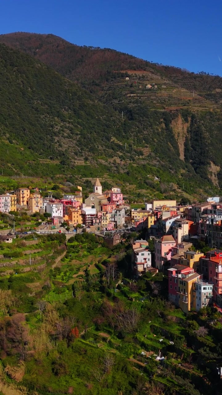Acercamiento vertical de dron hacia Manarola en Cinque Terre, Italia, en un día soleado, mostrando el estilo de vida costero y una vista panorámica del pueblo.