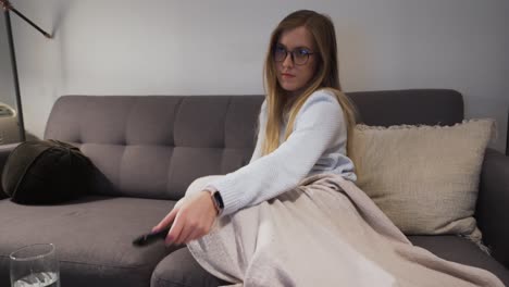 Girl-changing-channel-on-couch-curling-up-with-blanket