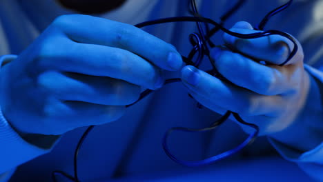 young woman trying to untangle the headphones in blue neon light close-up. tangled wires on table. trying to untangle many messy cables