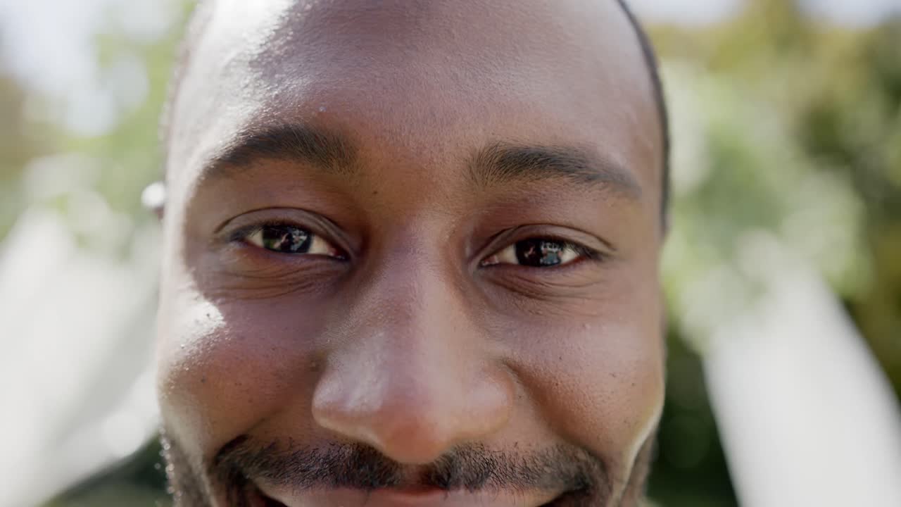 retrato en primer plano del feliz novio afroamericano sonriendo en una boda en un jardín soleado, en cámara lenta