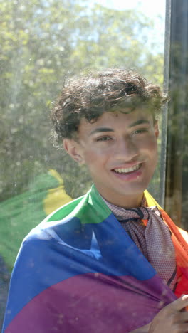 vertical video: smiling person wrapped in colorful flag, enjoying sunlight through window