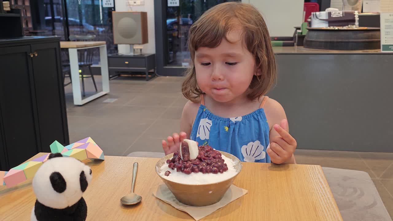 una niña linda tratando de comer un postre de hielo coreano con frijoles rojos dulces cubriendo