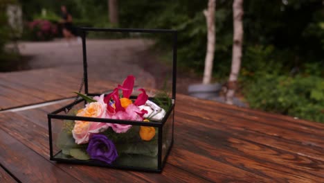 caja transparente abierta con flores de boda y anillos que descansan sobre la mesa