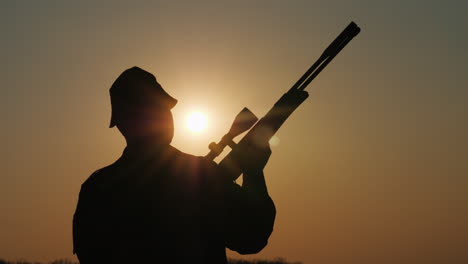 silueta de un cazador con un arma los rayos del sol brillan en su cara