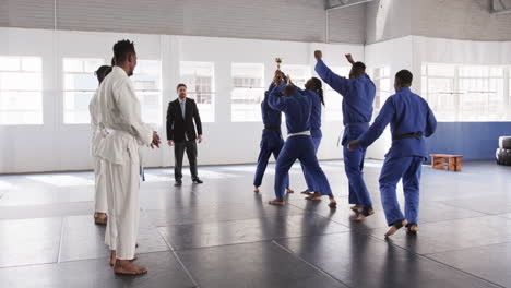 judo team celebrating victory with trophy in dojo, coach observing proudly